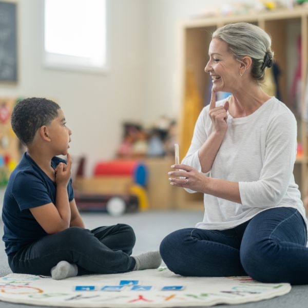 A therapist and a young boy sitting on the floor of a bright playroom