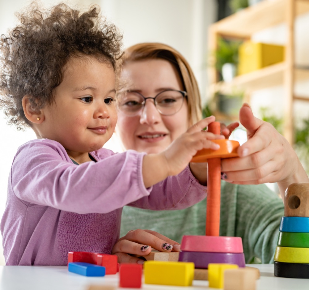 A smiling therapist and a toddler stacking colourful rings together